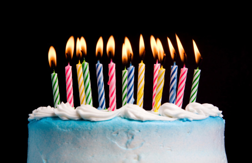 A birthday cake with lighted candles on a black background.  Shallow DOF with focus on the center row of candles.