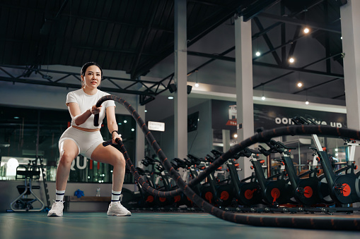 Young woman exercising with battle rope at the gym.
