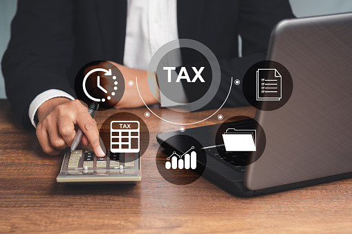 Tax day concept. An individual income tax payment form online. A Businessman in a suit using a calculator to calculate taxes while sitting in the office. Business icons on a virtual screen