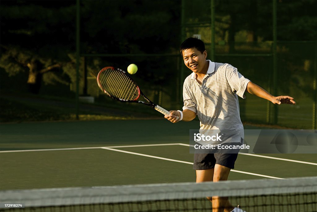 Net Play A male tennis player hitting a volley at the net. Asian and Indian Ethnicities Stock Photo