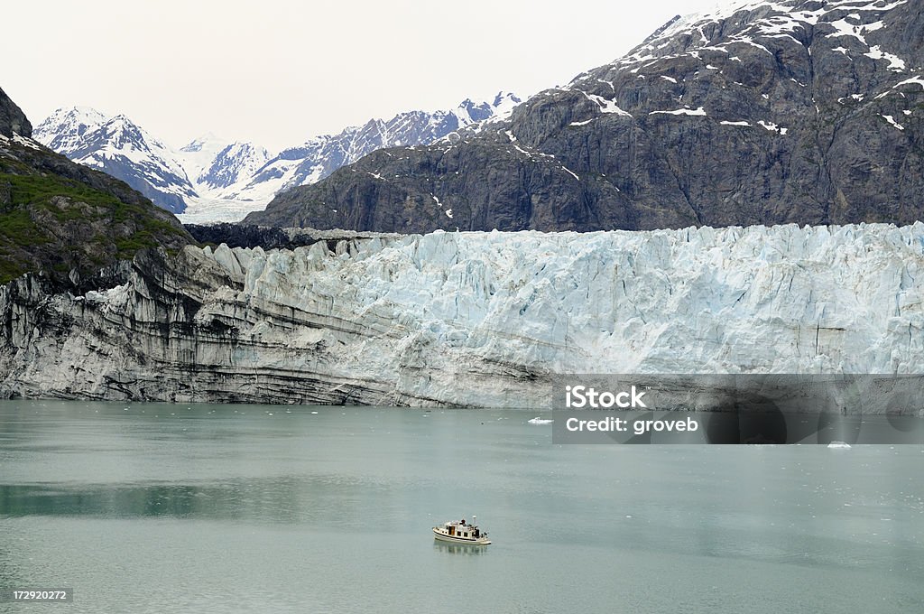 Boat dwarfed by large glacier. "A private tug boat is dwarfed by John Hopkins glacier in Glacier Bay National Park,Alaska." Alaska - US State Stock Photo