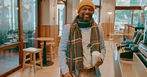Morning, portrait and a black man with coffee at a cafe for a break, weekend caffeine or relax. Happy, winter and an African person at a restaurant for a drink, latte or warm beverage takeaway