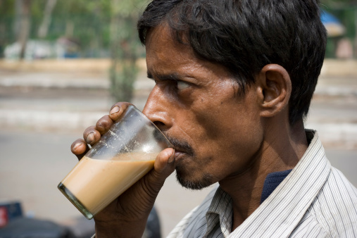 Rickshaw puller taking a break and having a glass of Tea at a road side tea stall in India