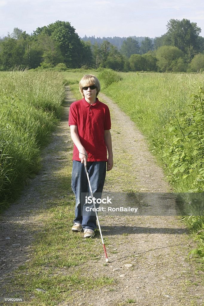 Cane Mobility on a Country Road A young cane-user walking along a country road. Blindness Stock Photo