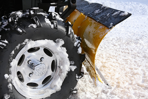 Plowing snow with a blade mounted on the rear of four-wheeler (ATV).  Close up.