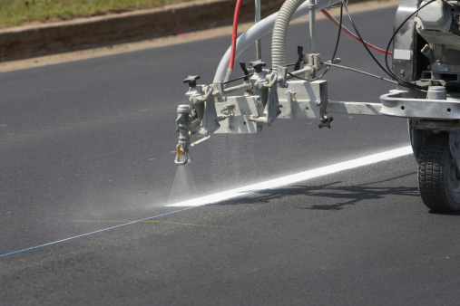 Pavement lane marker machine spraying a white stripe on a new asphalt road.