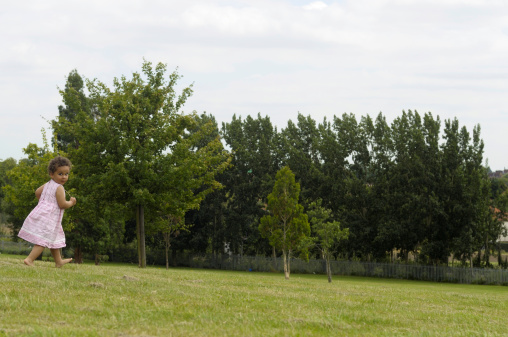 Two years old girl is running on grass barefoot.