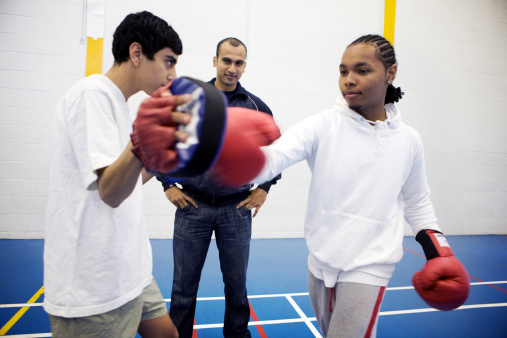 A pair of teenage students practice their boxing technique under the guidance of their coach.