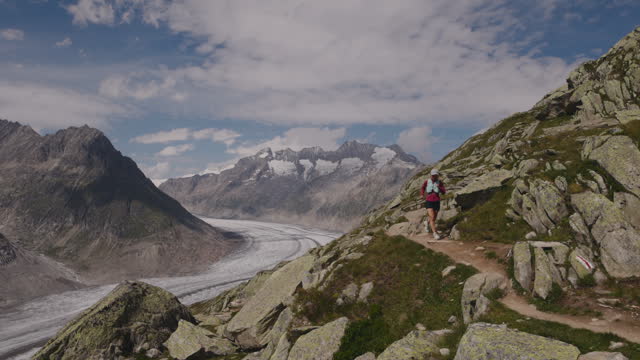 SLOW MOTION: Female trail runner ascends alpine path in Swiss mountain landscape