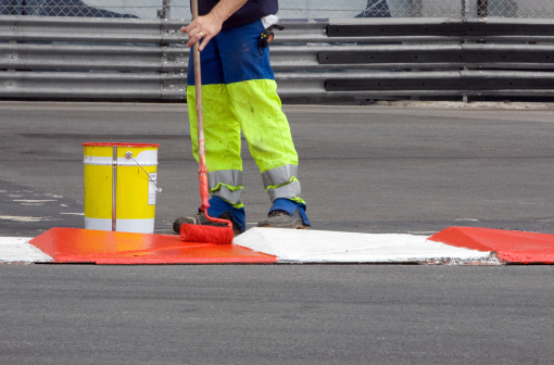 A municipal worker painting a red and white curb on a road.