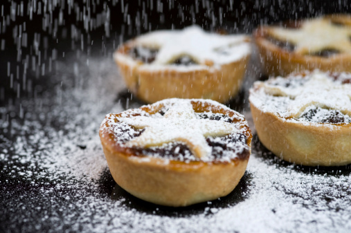 Homemade Christmas mince pies with falling icing sugar on black background.