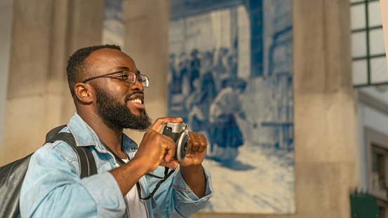 Smiling young african american man with cmera against classical azulejo wall. Travel in Portugal