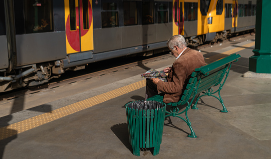 7 October 2022 - Porto, Portugal: A European Senior man sitting with the newspaper at the terminal train station.