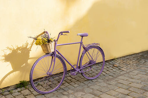 selective focus on lavender bicycle with flowers in a basket on yellow wall background