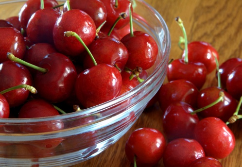 A bowl of cherries on oak table with selective focus