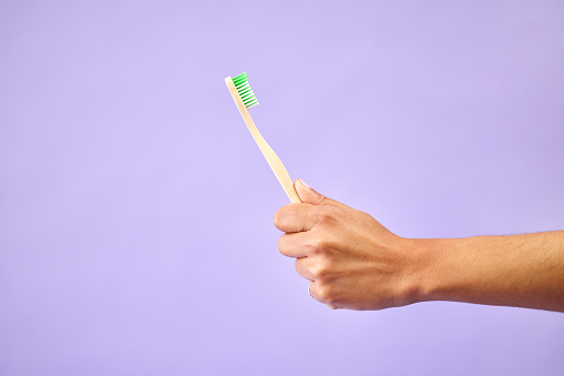Dental, teeth whitening and hand with toothbrush in studio for oral care, wellness and hygiene on purple background. Mouth, cleaning and person show bamboo tool for fresh breath, tooth or gum health