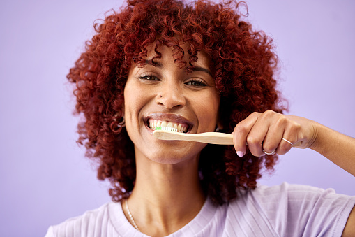 Face, smile and woman brushing teeth with bamboo in studio isolated on purple background. Portrait, wood toothbrush and happy person cleaning for eco friendly hygiene, dental health or sustainability