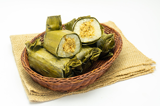 Indonesian tradisional food called lemper made from steamed glutinous rice with chicken meat wrapped with banana leaf, plate on rattan basket and isolated on white background