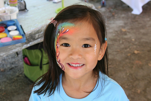 Adorable Chinese girl headshot with her face painted in vibrant colors