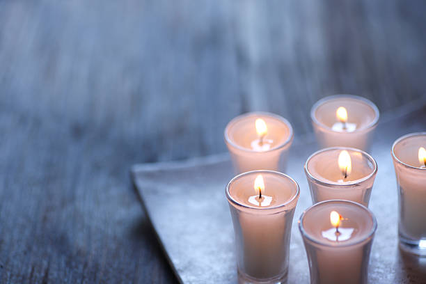 A group of small lit votive candles randomly placed on a plate. The plate sits on a distressed wooden surface. Shot with a very shallow depth of field. Ample copy space is provided in the negative space. A cool gray color scheme dominates the scene.