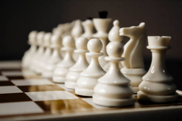 White chess in a row. Against the dark background, white chess stands out. Chessboard with white pieces. Chess is a battle strategy.
