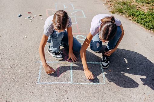 Cute girl drawing American flag with colored chalks on the sidewalk near the house on sunny summer day. Kids painting outside. Creative development of children. Patriotic day concept