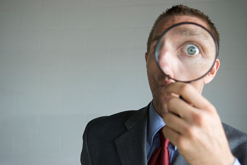 The surprise in the eye of a young man businessman is emphasized and enlarged by a magnifying glass