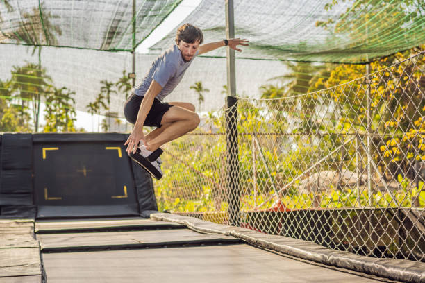 young man on a soft board for a trampoline jumping on an outdoor trampoline, against the backdrop of palm trees. the trampoline board is like a wakeboard, skateboard or snowboard trainer to hone your jumping skills - skateboard contest imagens e fotografias de stock