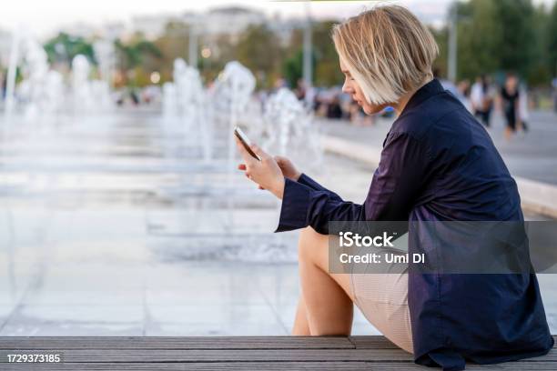 Walking In Thessaloniki Teen Girl Sitting At The Fountain And Scrolling Through The Information In The Phone On The Embankment Stock Photo - Download Image Now