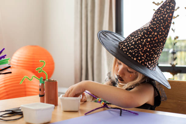 uma garota fofa em uma fantasia de bruxa faz uma aranha engraçada para o halloween com suas próprias mãos. artesanato infantil para o halloween - child autumn craft preschooler - fotografias e filmes do acervo