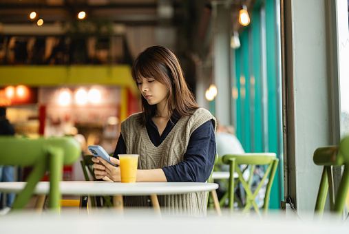 pretty young asian woman in a bar having a soft drink while looking at her smart phone