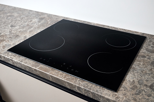 Flat cooktop cooking induction electric built black stove. Grey beige countertop with black glossy built in ceramic tempered glass induction or electric hob stove cooker with four burners, in kitchen.