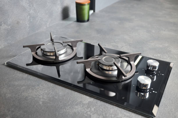 Contemporary tempered glass black gas stove hob with Two burners with auto ignition knob cast iron pan supports and flame safety valve, built in compact high pressure laminate HPL countertop. estufa de gas negra contemporánea de vidrio templado con dos quemadores con perilla de encendido automático, soportes para sartenes de hierro fundido y válvula de seguridad de llama incorporada en encimera compacta de hpl laminado de alta presión.