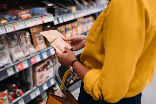 A side view of an unrecognizable Caucasian female holding some paper package at the grocery store and reading ingredients.