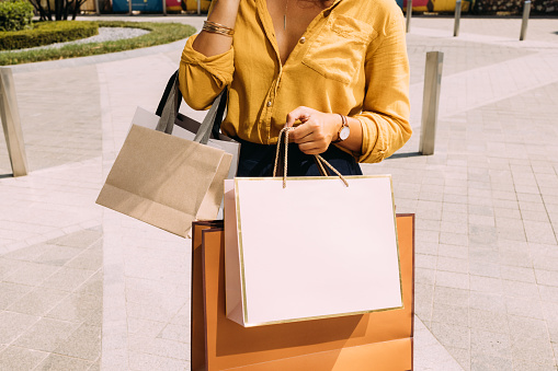 An unrecognizable Caucasian female with paper bags standing on the street agter going shopping.
