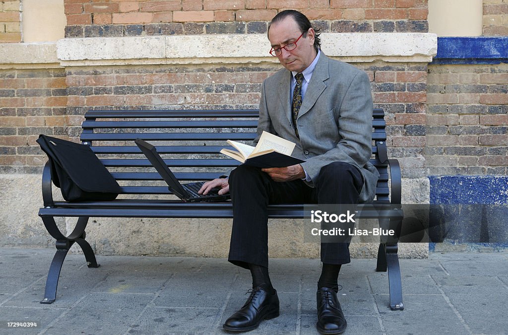 Biznesmen za pomocą laptopa i czytanie książki na ławce - Zbiór zdjęć royalty-free (Garnitur)