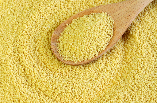 Uncooked dried couscous in wooden spoon. Durum wheat. Overhead view.