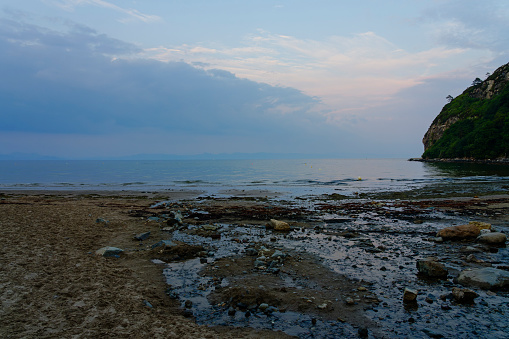 Rocks and stones litter a tidal pool on Llanbedrog beach at low tide on a summer evening.