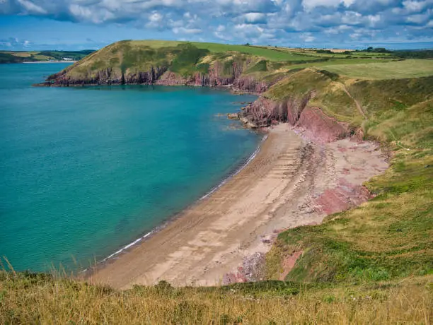 The red sand of the deserted Swanlake Beach in Pembrokeshire, Wales, UK. Taken from the coast path on a sunny day in summer with a turquoise sea.
