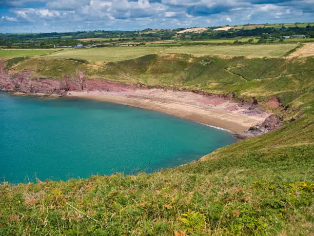 The red sand of the deserted Swanlake Beach in Pembrokeshire, Wales, UK. Taken from the coast path on a sunny day in summer with a turquoise sea.