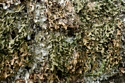 Camouflage netting in shades of green and brown hanging on a fence.More green or brown backgrounds: