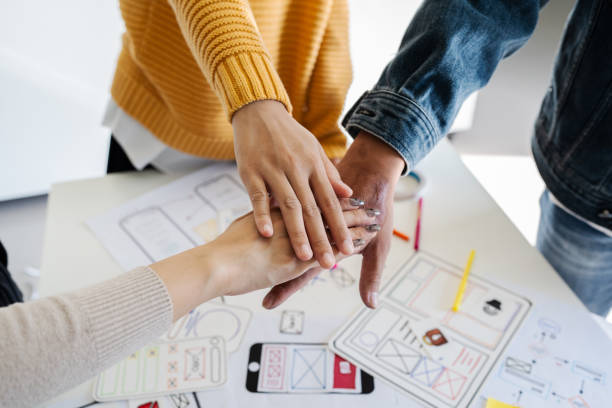 Asian ux developer and ui designer team stacking hands together, celebrating completion of project