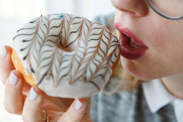 Close-up of a young woman's hand holding a doughnut and trying to eat it. stock photo