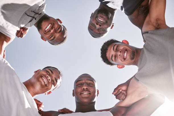 portrait of sporty men from below joining in huddle for support and unity. group of cheerful friends and motivated athletes collaborating together in solidarity as a happy team and diverse community - exercising motivation looking up african descent imagens e fotografias de stock