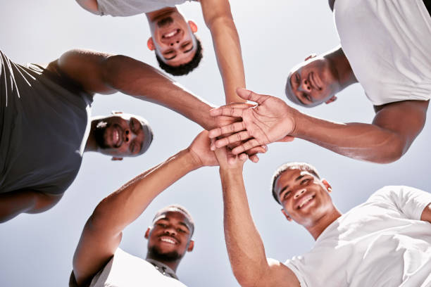 portrait of sporty men stacking hands in a huddle for team support, collaboration and unity from below. group of cheerful and motivated athletes joining together in a circle for  encouraging pep talk - exercising motivation looking up african descent imagens e fotografias de stock