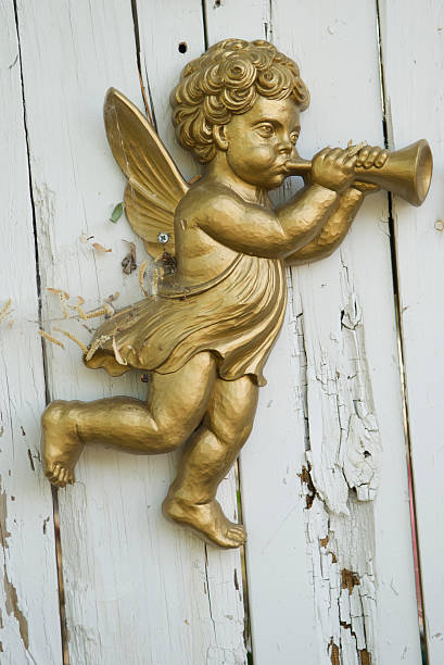 Gold painted angel cherub statue blowing his horn hanging from an old white fence