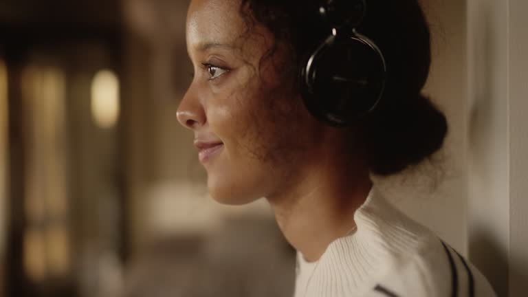 Young woman listening to music at home, leaning against a wall