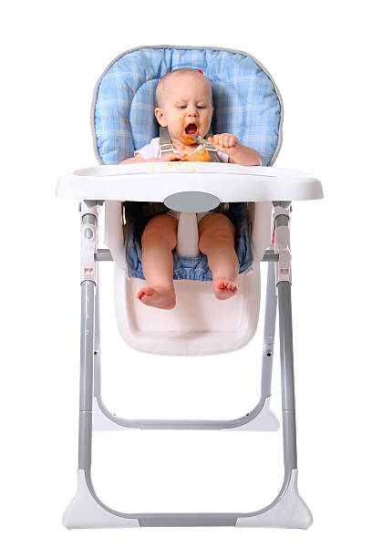 little boy in bib eating bagels and sitting in highchair isolated on white background