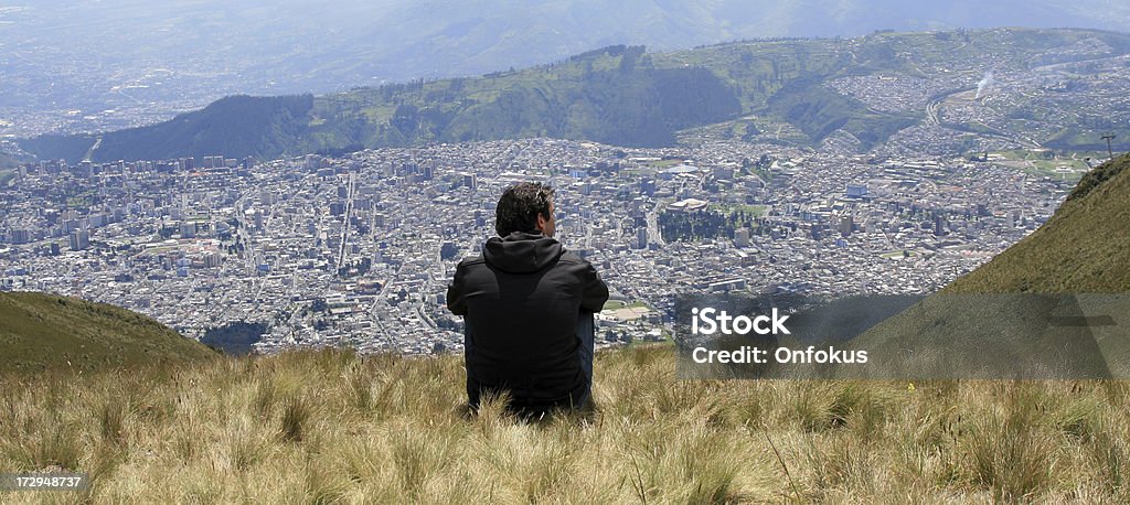 男性が座っている山の山頂、エクアドルの首都キトの街 - キトのロイヤリティフリーストックフォト
