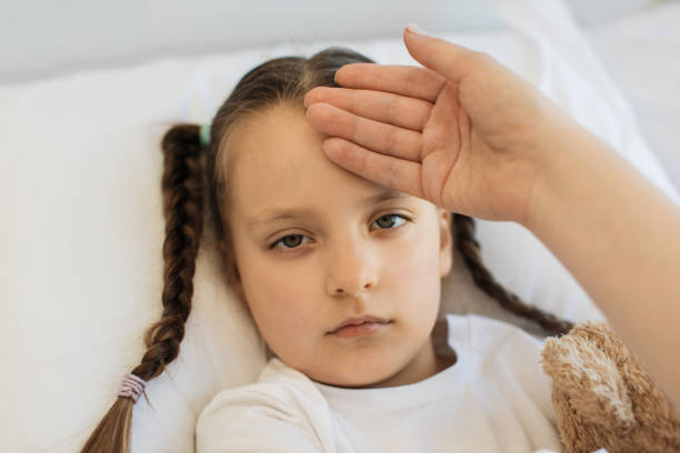 istock Sick girl resting in bed with mother's hand on forehead 1729497634